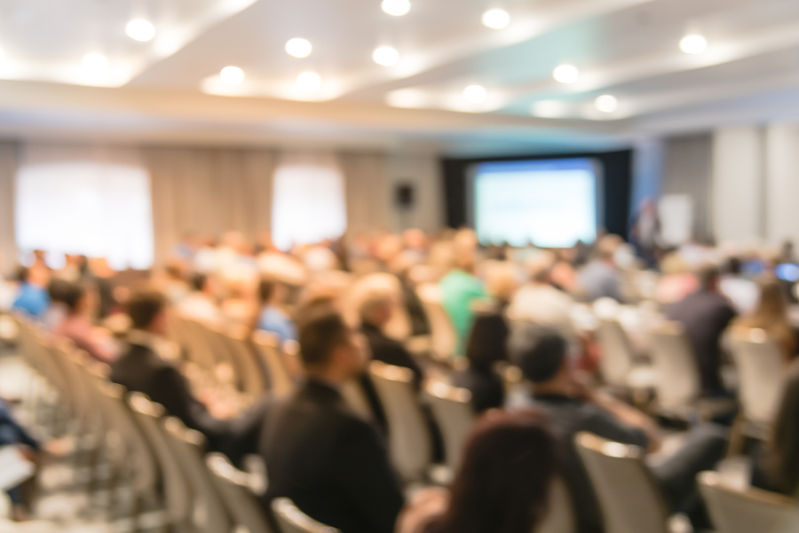 blurry-background-speaker-on-conference-stage-with-projector-in